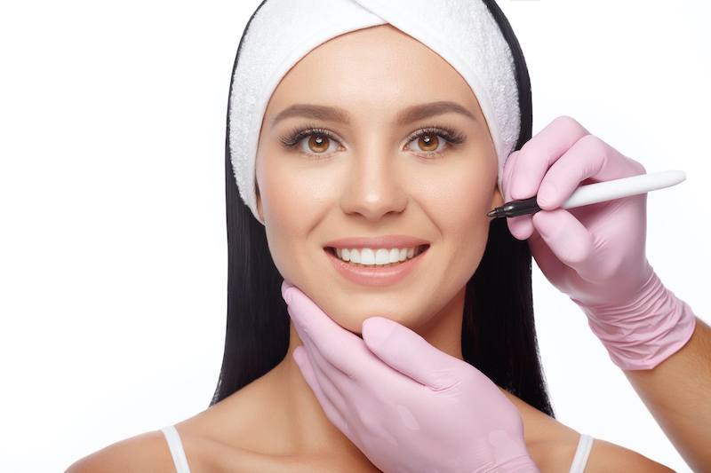 Young woman before plastic surgery operation. Beautician touch and draw correction lines on woman face. Woman face plastic operation. Beauty Face. Aesthetic face